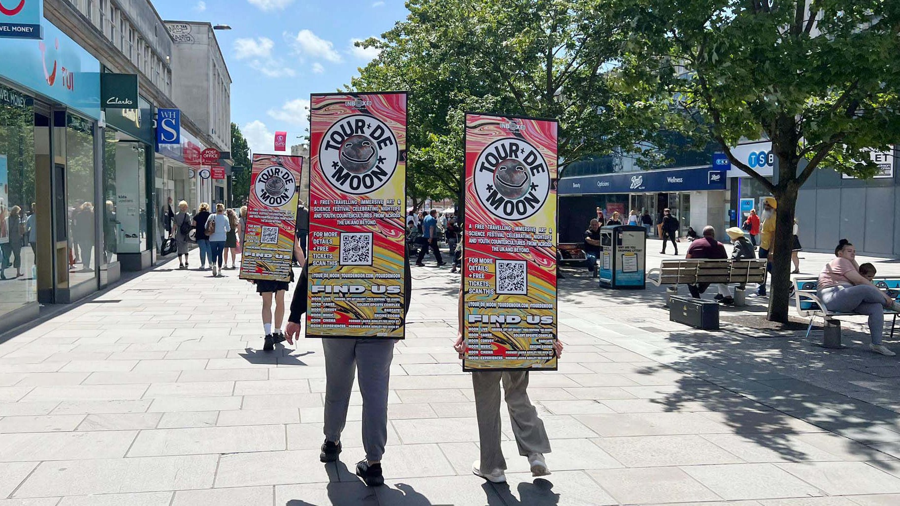 Three people walking with Tour De Moon Advert Walker boards on the high street